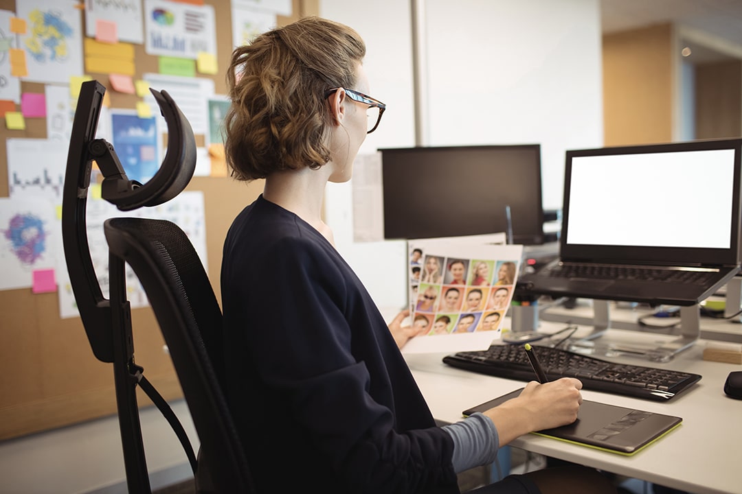 Top underrated office supplies including an ergonomic chair and laptop riser, boosting productivity for a woman at a modern desk